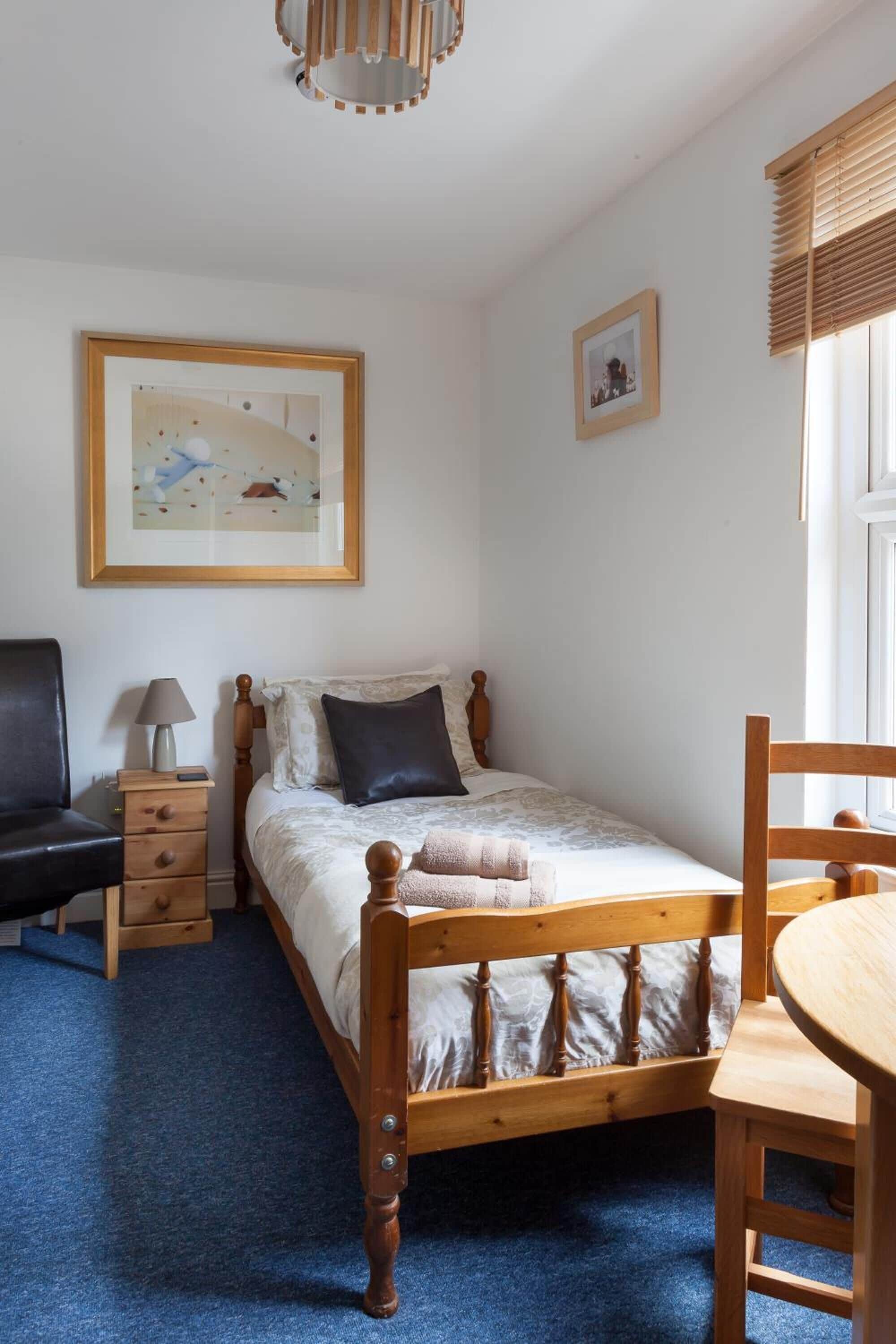 A bedroom with a wooden bed, a bedside table with a lamp, a chair, and a small table.