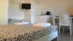 Una habitació d'hotel amb llit, escriptori, cadira, televisió penjada a la paret i un armari.