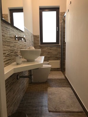 A narrow bathroom with a stone backsplash, a white sink, a white toilet, and a bathtub. - Dependance tra gli ulivi (Ostuni)