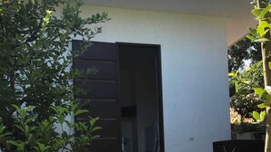 Un edifici amb una porta oberta a mig fer, envoltat de vegetació i un camí de terra.
