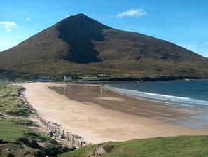 Una playa con una montaña al fondo, casas a lo largo de la costa y una valla a lo largo de la orilla.