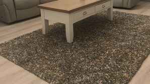 Een woonkamer met een beige bank, een fauteuil, een salontafel en een klein vloerkleed.