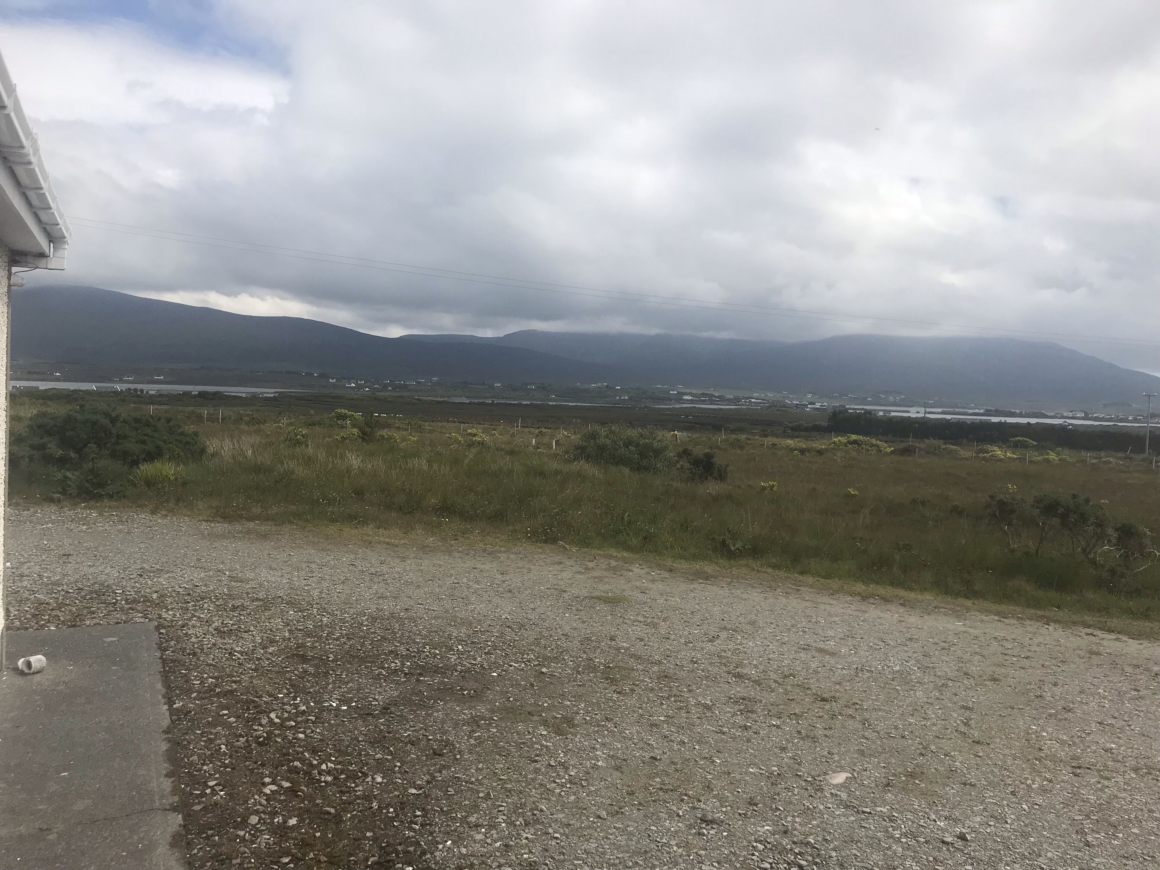 En grusväg med en gräsbevuxen äng och berg i fjärran.