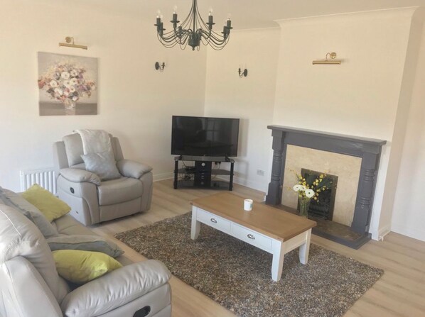 A living room with a grey sofa, a coffee table, a TV, a fireplace, and a chandelier.