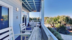 A covered outdoor area with wooden benches and a railing, overlooking a landscaped garden with palm trees. - Bay View Villas 105 | Waterfront, Community Pool (Tybee Island)
