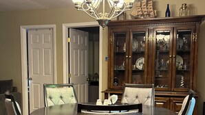 Uma sala de jantar com uma mesa redonda, seis cadeiras, um candelabro e um aparador de madeira com portas de vidro.