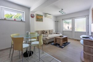 A modern living room with a glass dining table, yellow chairs, a beige sofa, and a small wooden side table.