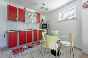 A compact kitchen with red cabinets, a glass-top dining table, and yellow chairs.