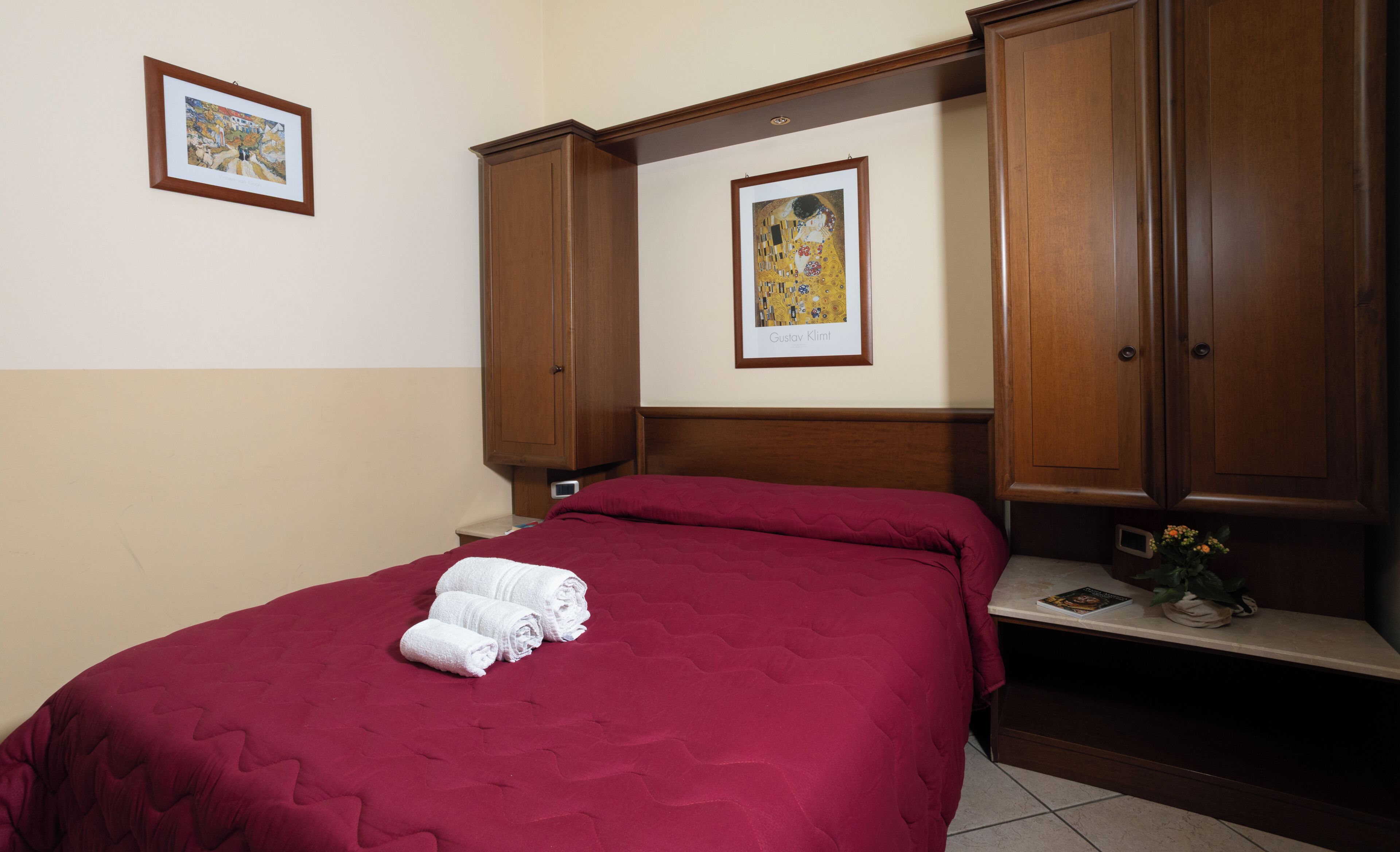 Habitación de hotel con cama, armario de madera y dos cuadros enmarcados en la pared.