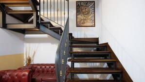 A staircase with wooden steps and metal railings, a red leather sofa, and a framed artwork on the wall. - Hotel Gangi (Piazza Armerina)