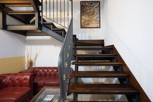 Una escalera con escalones de madera y barandillas metálicas, un sofá de cuero rojo y una obra enmarcada en la pared.