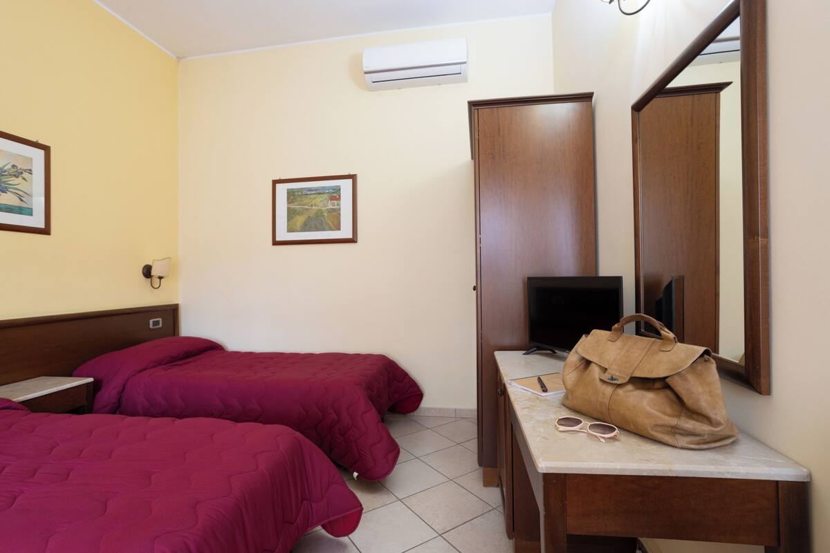 A hotel room with two beds, a desk, a mirror, and a TV.