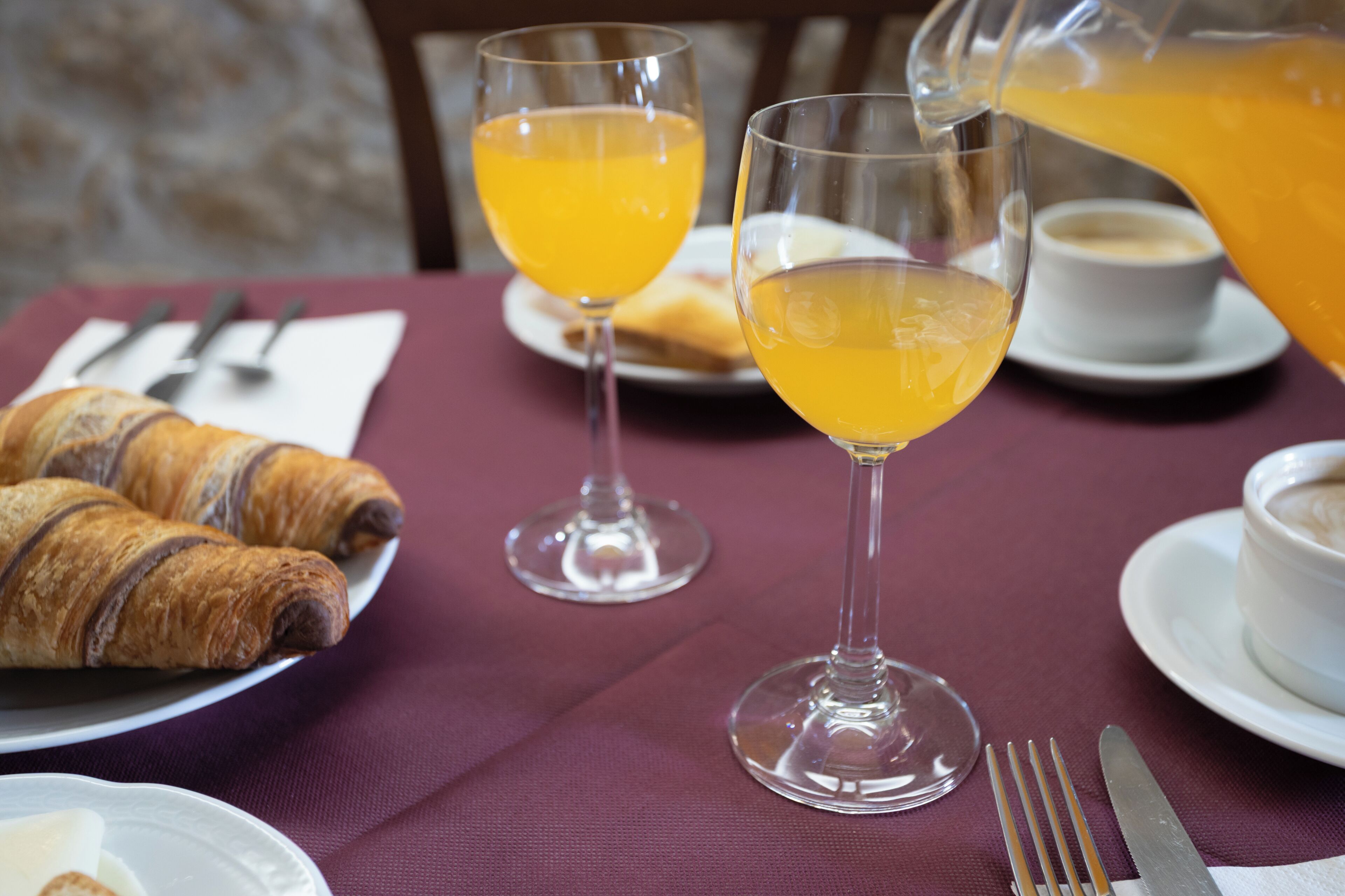 Een tafel met croissants, glaasjes sinaasappelsap, een koffiekop en een kan sinaasappelsap.