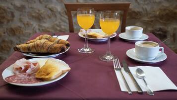 Frühstückstisch mit Croissants, Toast, Schinken und Käse, dazu zwei Gläser Orangensaft und eine Tasse Kaffee.