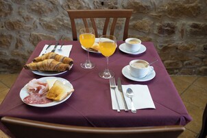 Una mesa dispuesta con croissants, tostadas, jamón, queso y una taza de café, junto con dos vasos de zumo de naranja.