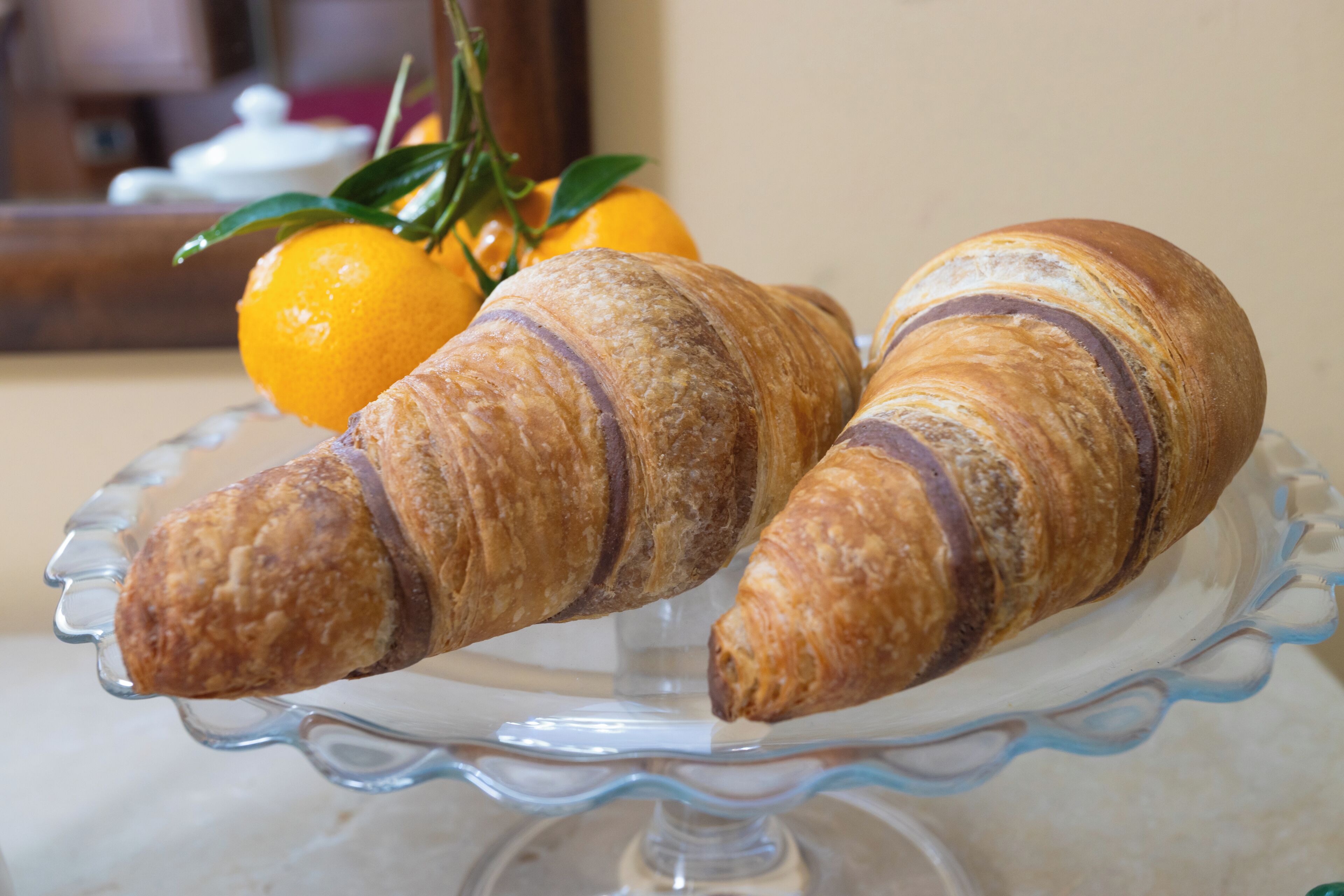 Zwei Croissants auf einer Glaskuchenplatte vor unscharfem Hintergrund.