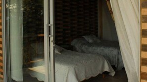 A bedroom with a sliding glass door leading to a balcony, a bed with a white bedspread, and a window with curtains.