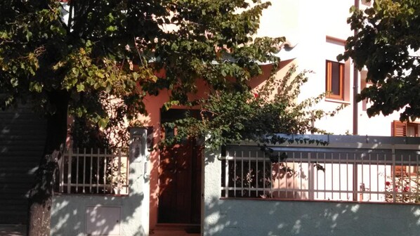 A building with a gated entrance, a mailbox with the number 73, and a tree partially obscuring the view. - Bed and Breakfast L'Abete (Guspini)