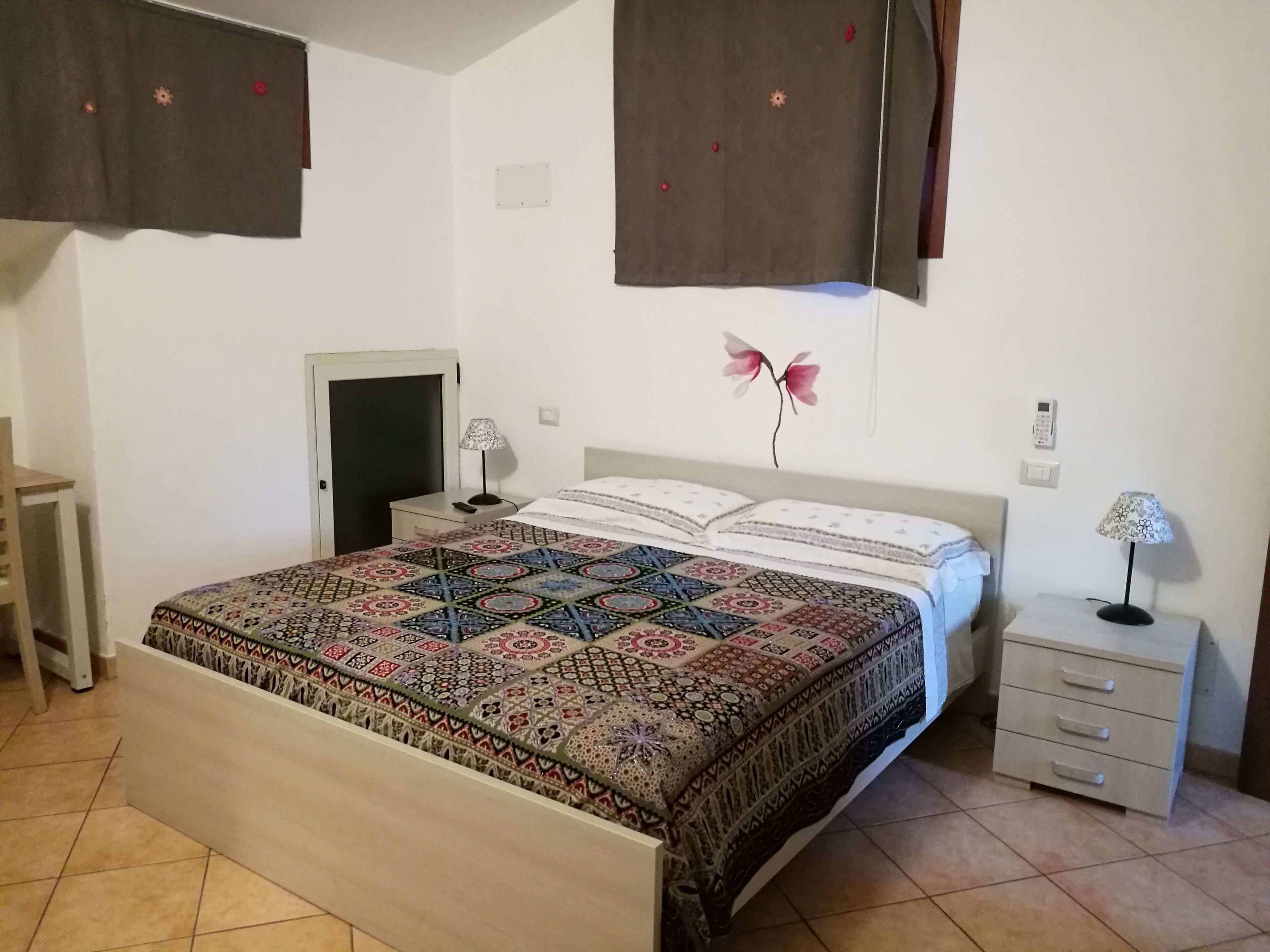 A bedroom with a bed, nightstands, a desk, and a door.