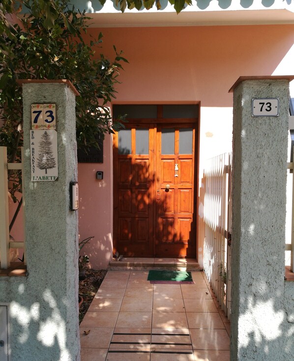 Una puerta de madera con un panel de vidrio, un felpudo verde en la entrada y el número 73 en un pilar.