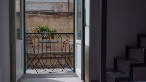 Ein Balkon mit Tisch, Stühlen, einem Blumentopf und einer Weinflasche.