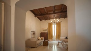 Ein Wohnzimmer mit einer Couch, einem Couchtisch, einem Esstisch mit Stühlen, einer Deckenleuchte und einem Fenster mit Vorhängen.