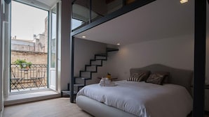 Ein Schlafzimmer mit Bett, einer Treppe und einem Balkon mit Gartenmöbeln.