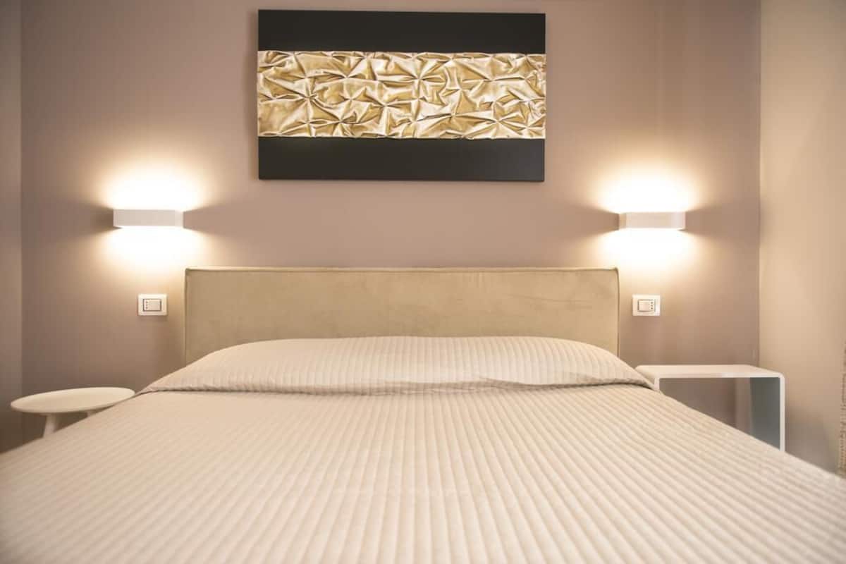 A neatly made bed with a headboard, two bedside tables, and wall-mounted lighting.