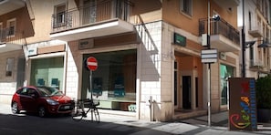 A red car parked on the street in front of a building with a 'BPER' sign, a no entry sign, and a 'Gecara Shopping Village' sign. - Casa Gaia (Pescara)
