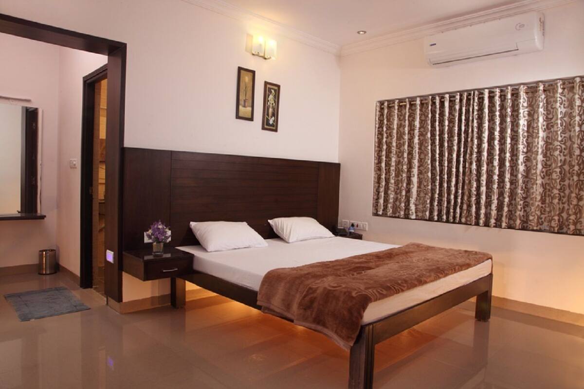 Une chambre d’hôtel avec un grand lit, une tête de lit en bois, une table de chevet avec une lampe et un climatiseur fixé au mur.