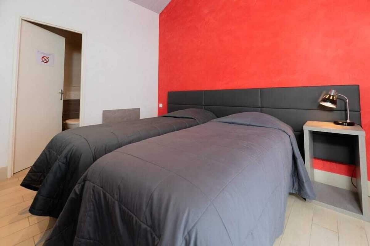 A room with two beds, a red accent wall, a black headboard, and a bedside table with a lamp.
