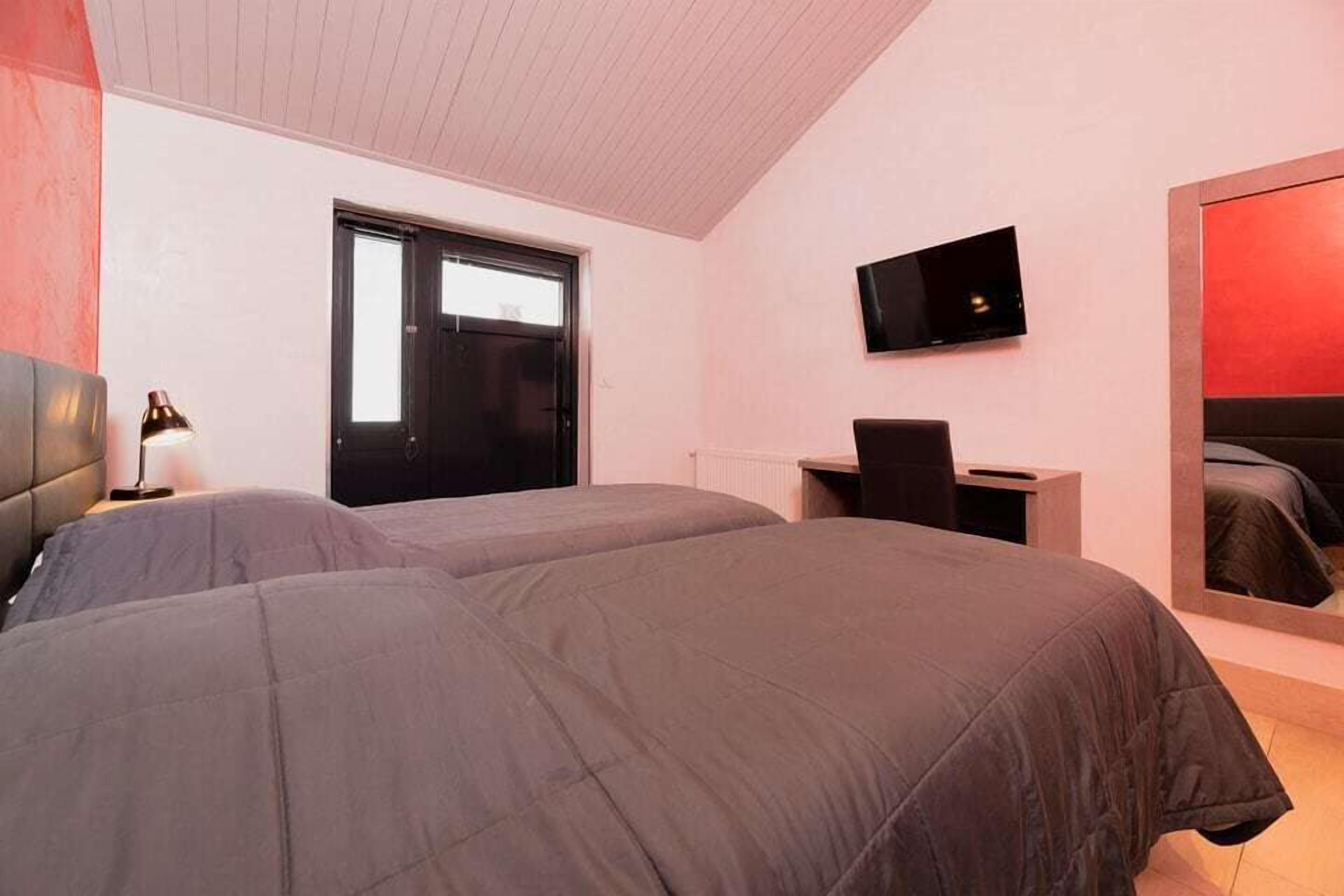 A bedroom with two beds, a desk, a chair, a TV, and a large window.