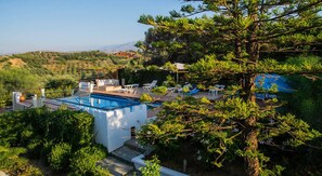 A pool area with lounge chairs and a pergola, surrounded by greenery and overlooking a hilly landscape. - Villas Eva with Panoramic Sea view (Chania)