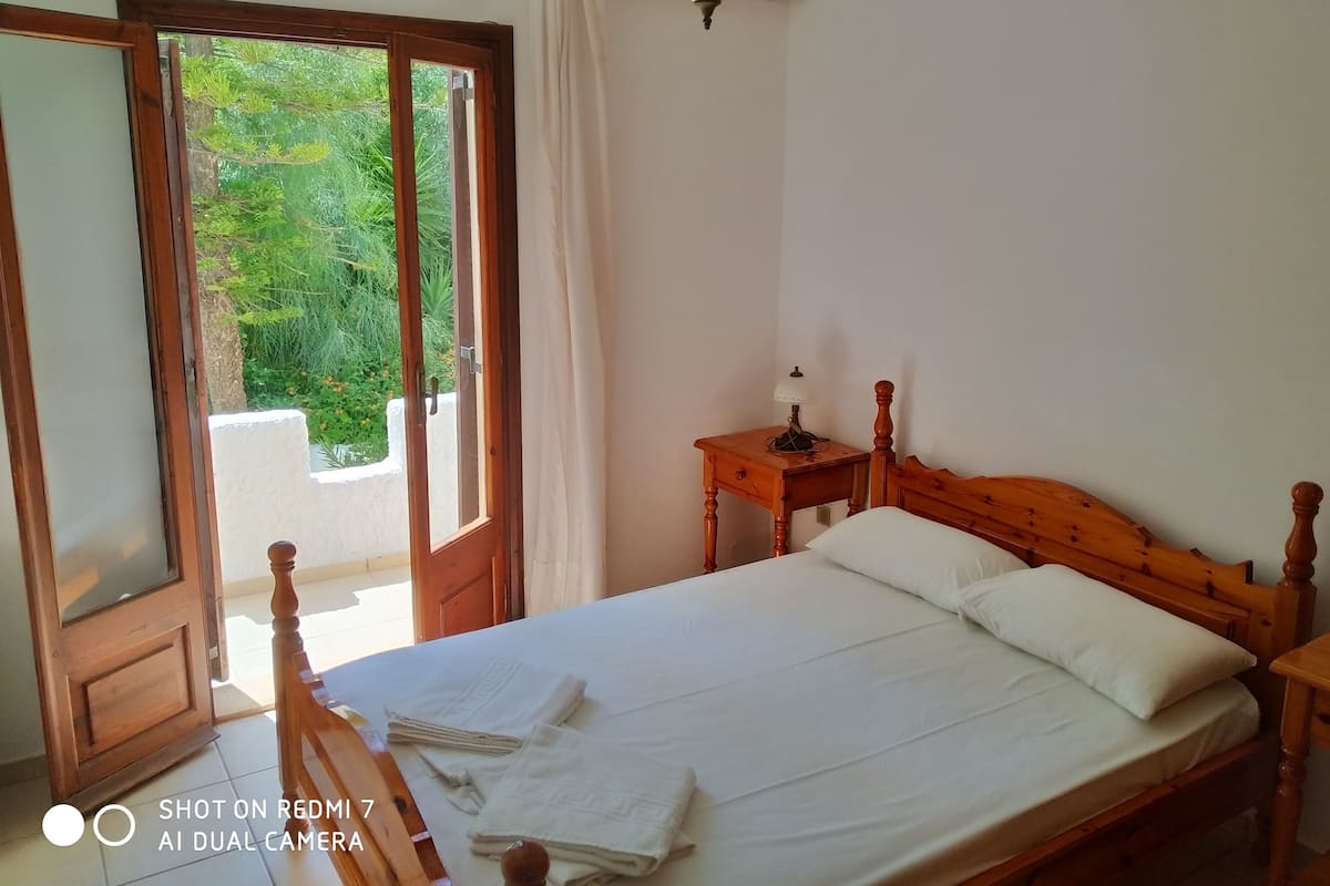 Une chambre à coucher avec un lit en bois, une table de chevet, une lampe et une fenêtre avec des rideaux.