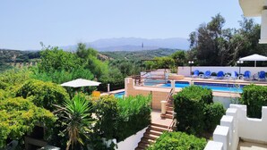 Uma área de piscina com cadeiras de descanso azuis, rodeada por vegetação exuberante e vista para montanhas ao longe.