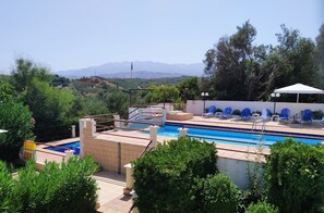 A swimming pool with a view of mountains, surrounded by greenery and blue chairs. - Villas Eva with Panoramic Sea view (Chania)