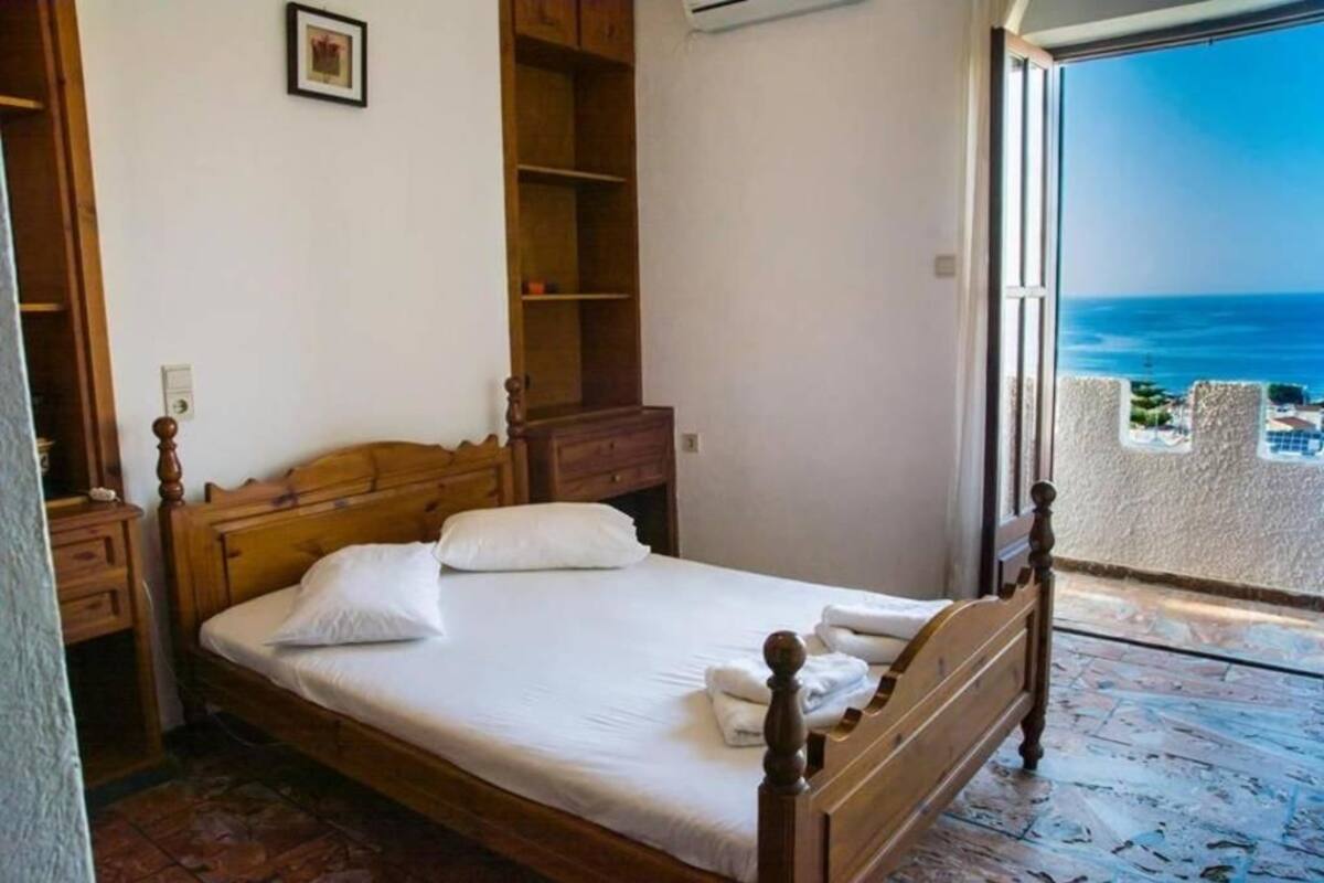 Une chambre à coucher avec un lit en bois, une table de chevet, une armoire et un balcon donnant sur la mer.
