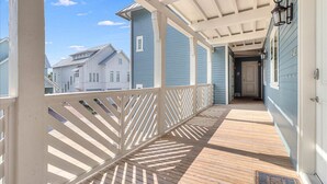 A covered porch with a wooden floor and white railings, leading to a door with a doormat. - Great Location@Cinnamon Shore Condo w/ Modern Style & Great Amenities! (Port Aransas)