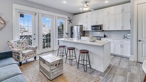 A modern kitchen with white cabinets, a central island with stools, and a ceiling fan. - Great Location@Cinnamon Shore Condo w/ Modern Style & Great Amenities! (Port Aransas)