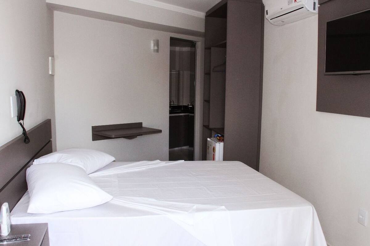 A hotel room with a bed, a bedside table, a phone, and a TV mounted on the wall.