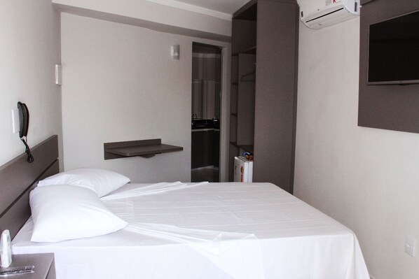 Habitación de hotel con cama, mesita de noche, teléfono y televisor montado en la pared.