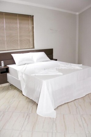Una cama bien hecha con sábanas blancas en un dormitorio moderno con cabecera de madera y una mesita de noche.