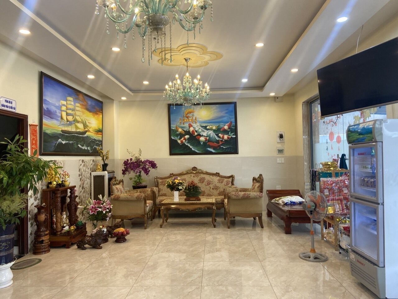 A spacious lobby with a chandelier, a sofa set, a coffee table, and a refrigerator stocked with items.