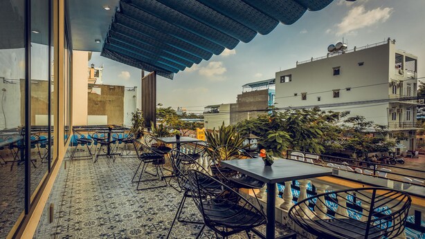 Un espacio de estar al aire libre con baldosas de suelo estampadas, sillas de metal y un toldo azul.