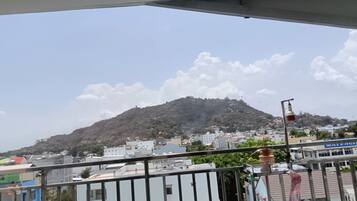 A view from a balcony overlooking a cityscape with a hill in the distance, buildings, and a clear sky.