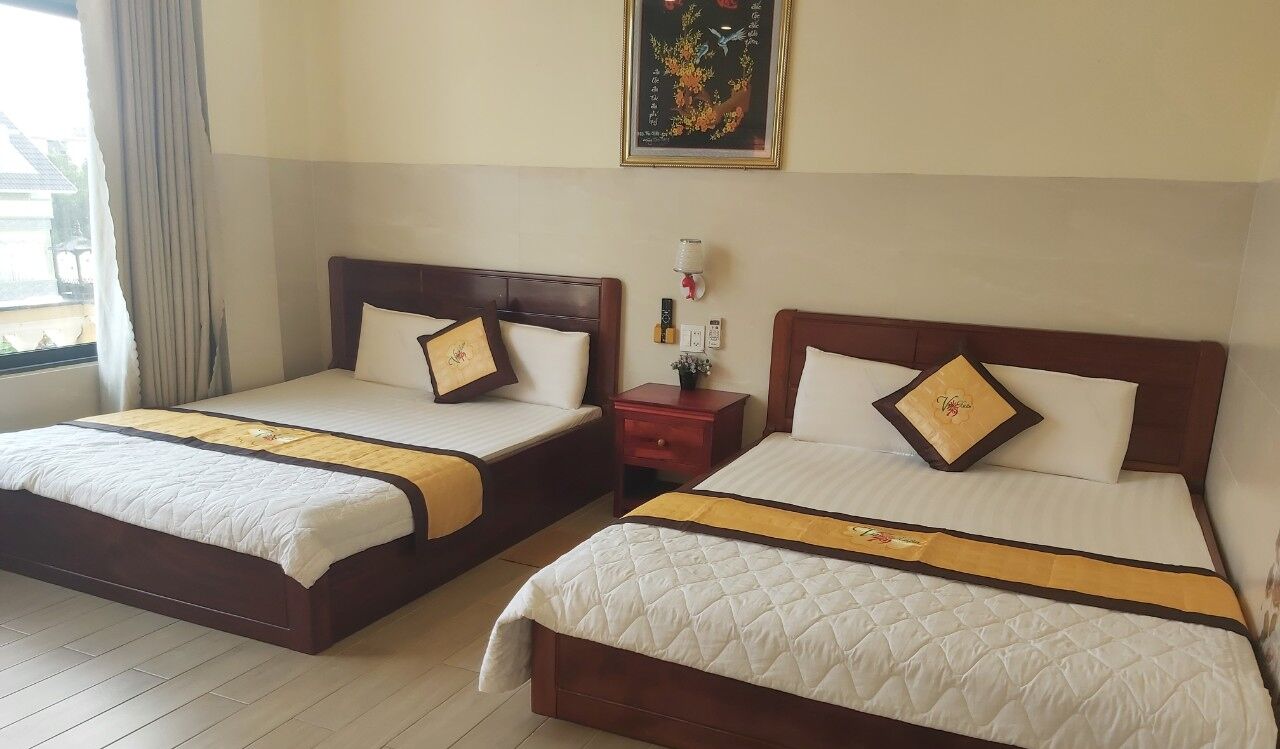 Dos camas dobles con cabeceros de madera y ropa de cama blanca, una mesita de noche con lámpara, y un cuadro enmarcado en la pared.