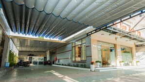 Fachada de un hotel con un espacio exterior cubierto, una recepción visible y una motocicleta estacionada afuera.