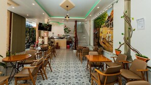Un restaurante con suelo de baldosas, mesas y sillas de madera, una zona de bar y una escalera que conduce a un nivel superior.