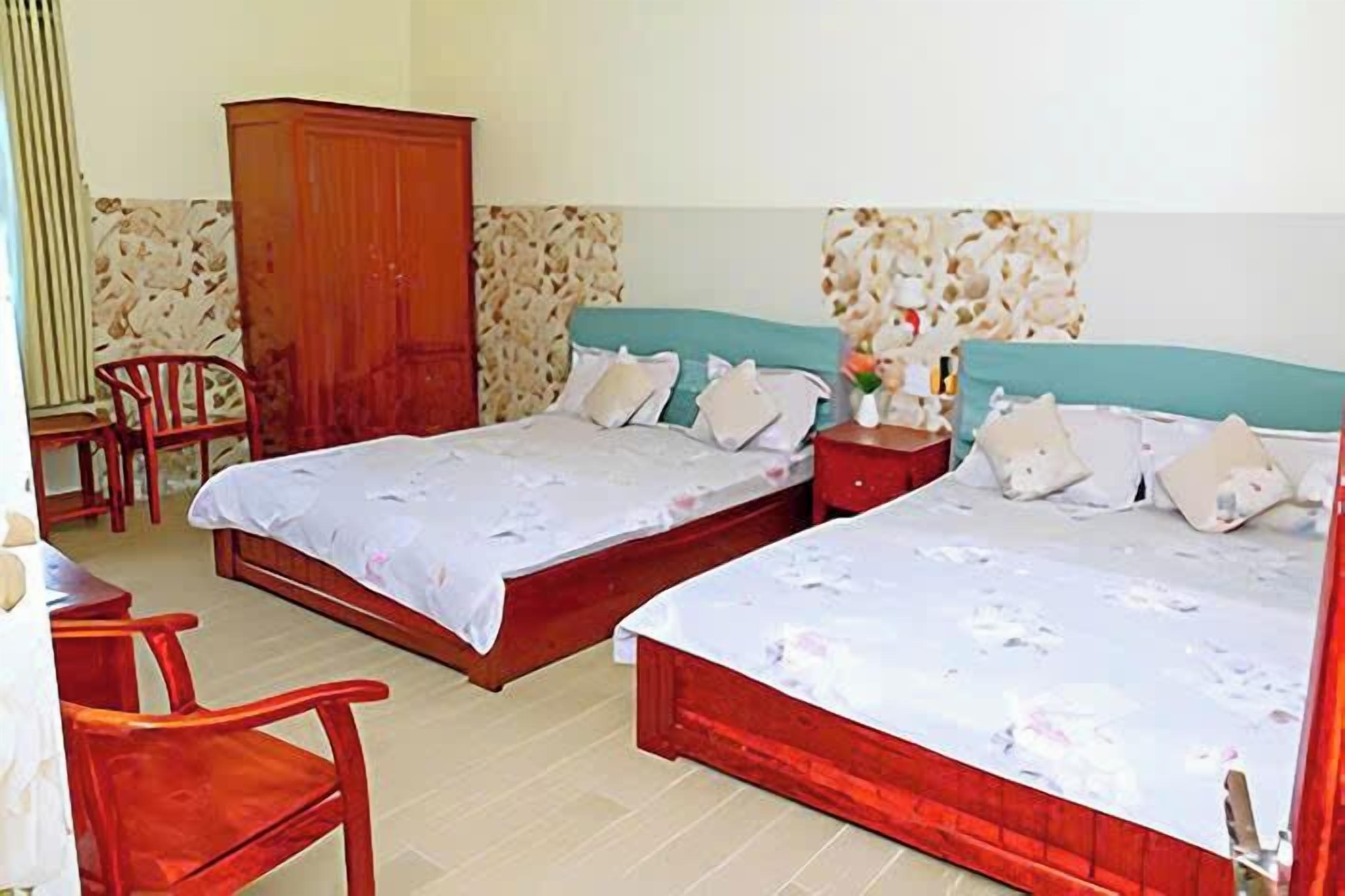 A room with two beds, a wooden wardrobe, a desk, and a chair.