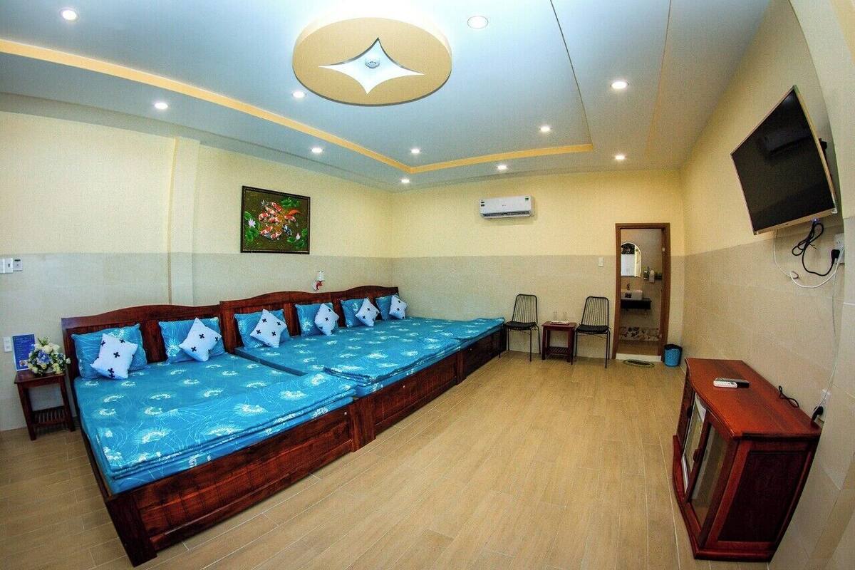 A large room with a long bed, a television mounted on the wall, and a ceiling light fixture.